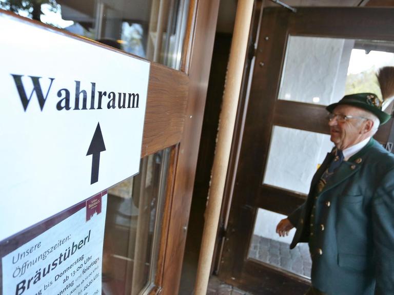Ein älterer Wähler betritt die Tür zum Wahllokal. Er trägt einen Hut mit Gamsbart.