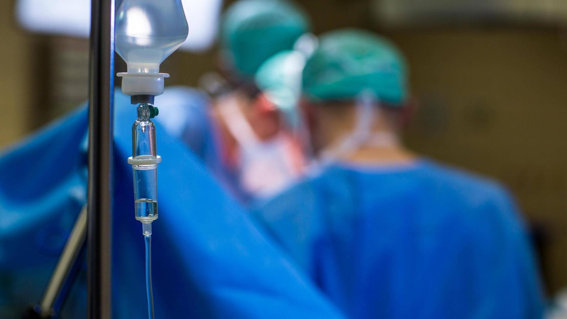 Ärzte bei einer Operation, im Vordergrund ein Tropf Ärzte bei einer Operation, im Vordergrund ein Tropf