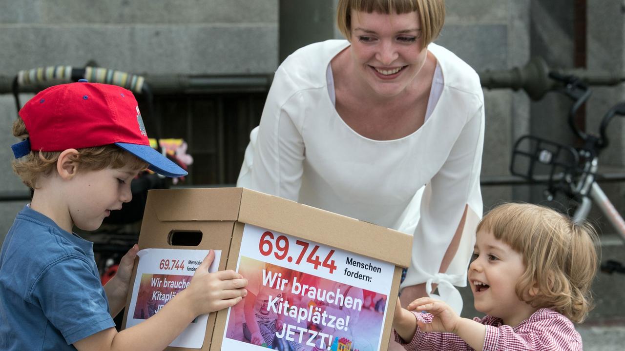 Katharina Mahrt vom Eltern-Bündnis "Kita Krise Berlin" stapelt mit zwei Kindern die symbolischen Kartons mit einer Petition für mehr Kitaplätze in Berlin. 