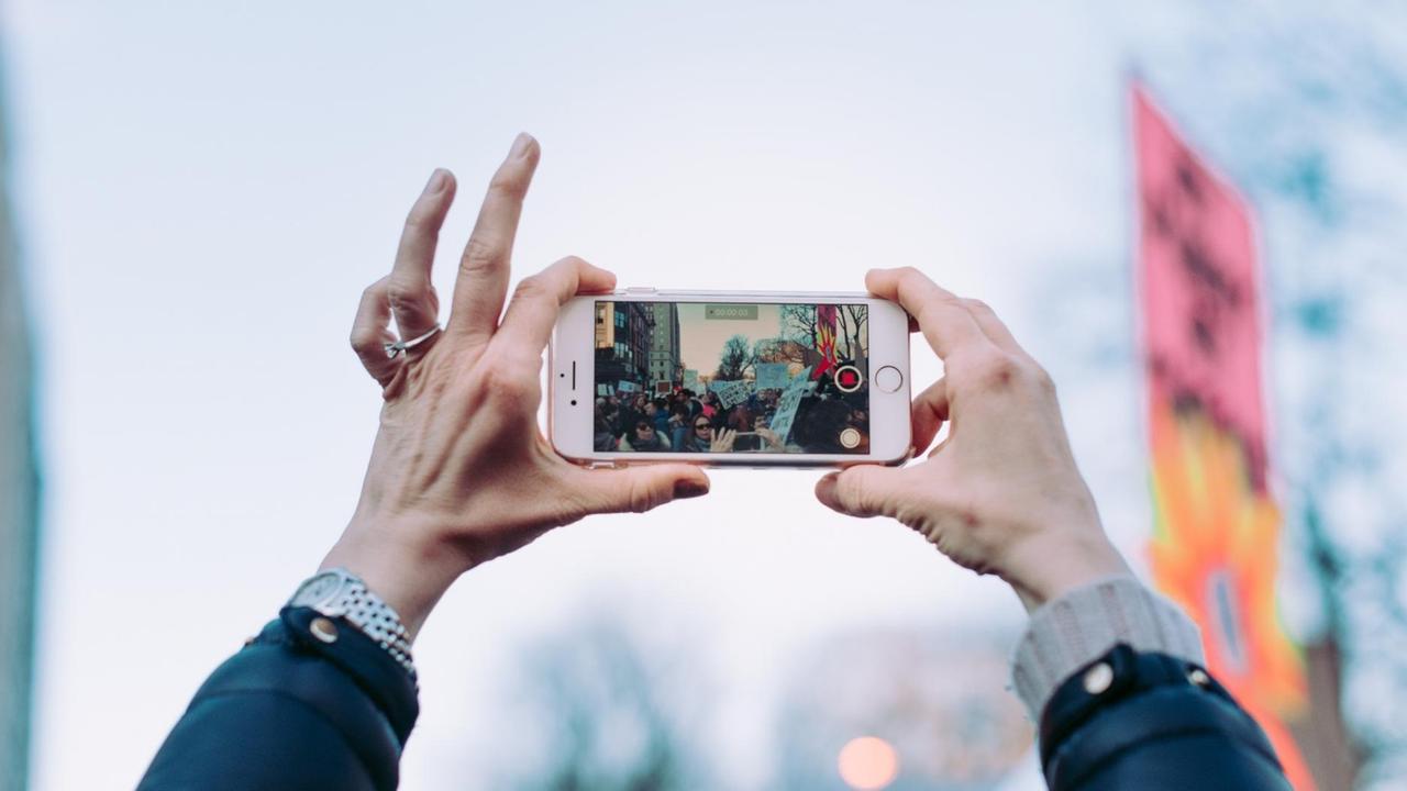 Eine Frau filmt mit einem Smartphone einen Demonstrationszug. Eine Frau filmt mit einem Smartphone einen Demonstrationszug.