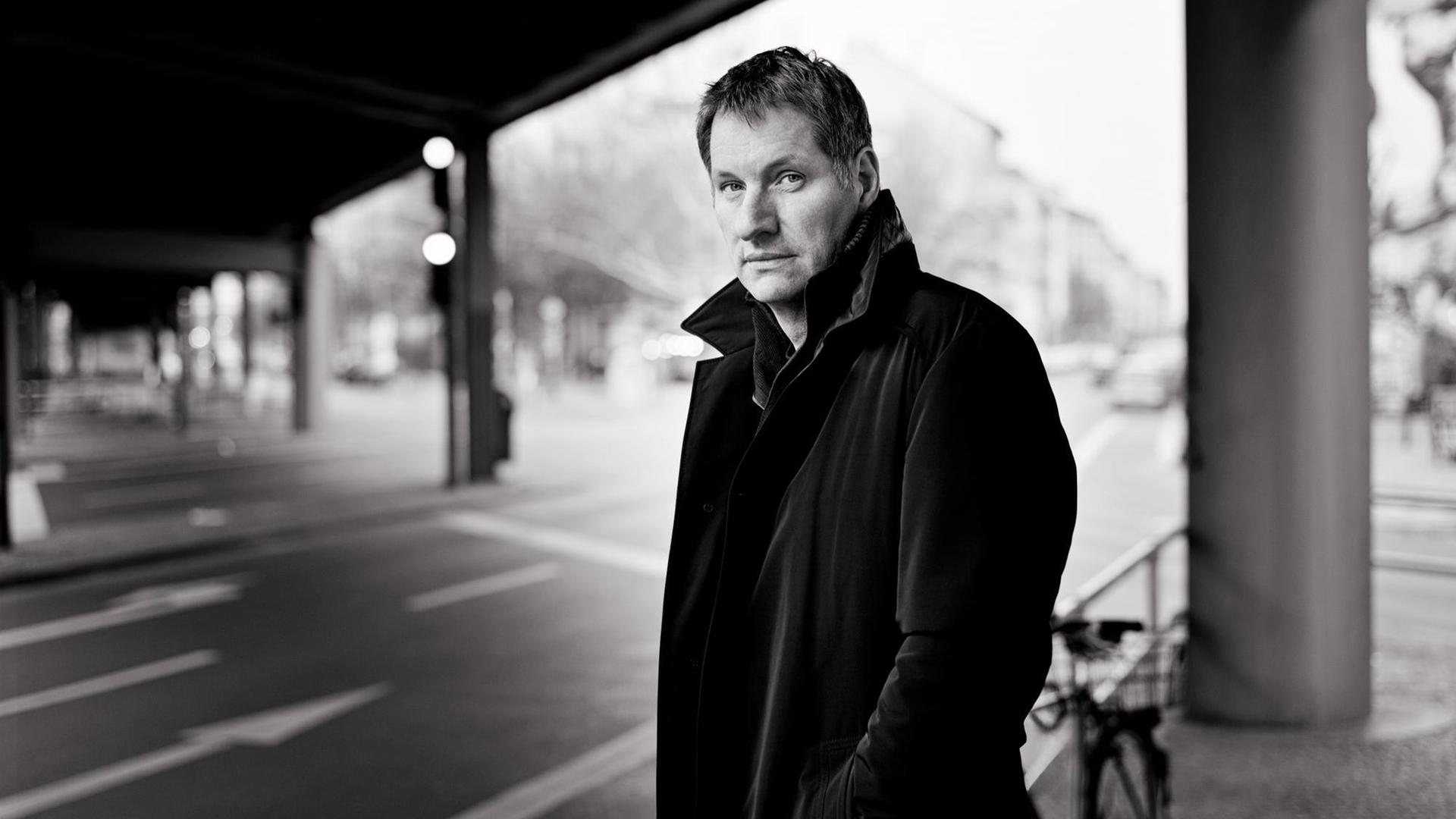 Marcus Wiebusch steht in einem dunklen Mantel unter einer Brücke an einer Strassenkreuzung. Marcus Wiebusch steht in einem dunklen Mantel unter einer Brücke an einer Strassenkreuzung.