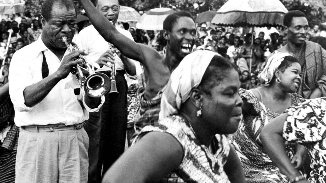 Frauen und Männer tanzen in afrikanischer Kleidung, während etwas im Hintergrund Louis Armstrong Trompete spielt.