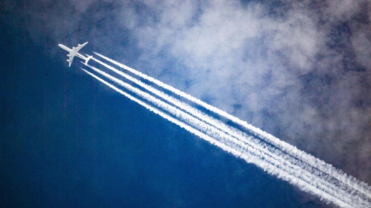 Ein Flugzeug zieht Kondensstreifen hinter sich her, während es durch die Wolken fliegt.