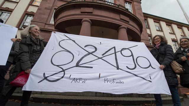 Mit einem Transparent fordern Demonstranten in Gießen die Abschaffung des Paragrafen 219a.