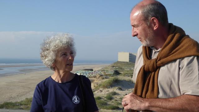 Die Umweltschützer Maryse Sinsout und Denis Trioulaire diskutieren am Strand von Soulac-sur-Mer über die fortschreitende Erosion. In ihrem Rücken sind ein Wehrmachtsbunker und der Wohnblock „Le Signal“ zu sehen. Das vierstöckige Haus droht auf den Strand zu kippen.