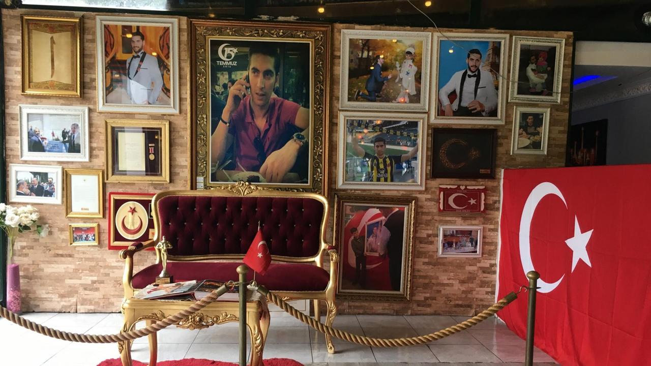 Die Gedenkstätte im Istanbuler Café Tolga. An einer Wand hängen viele Bilder des Verstorbenen Tolga Ecebalin, Türkei-Fahnen und eine Urkunde.