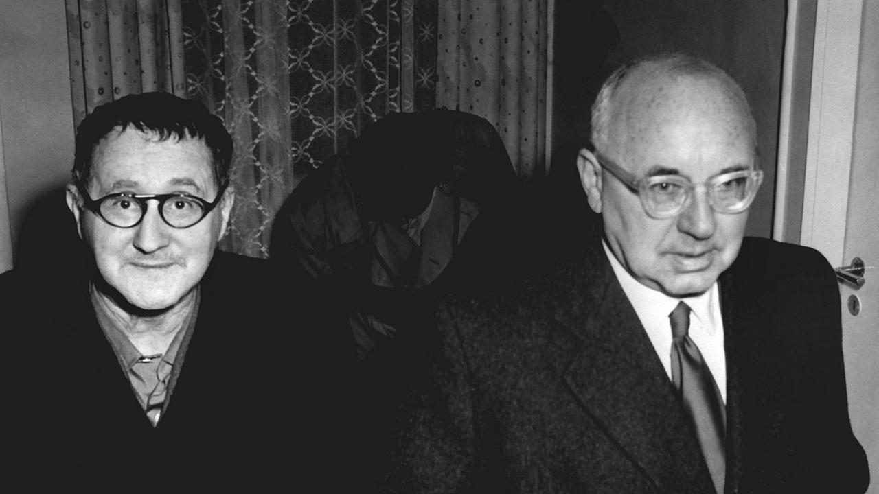 Eine schwarz-weiß-Fotografie zeigt Bertolt Brecht und Johannes R. Becher, wie sie 1954 gemeinsam durch ein Hotelzimmer laufen.