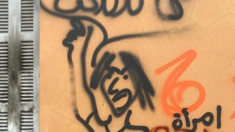 Ein schwarzes Graffiti auf einer gelben Hauswand zeigt eine wützende Frau, die ruft: "Wir werden nicht still sein“ Ein schwarzes Graffiti auf einer gelben Hauswand zeigt eine wützende Frau, die ruft: "Wir werden nicht still sein“