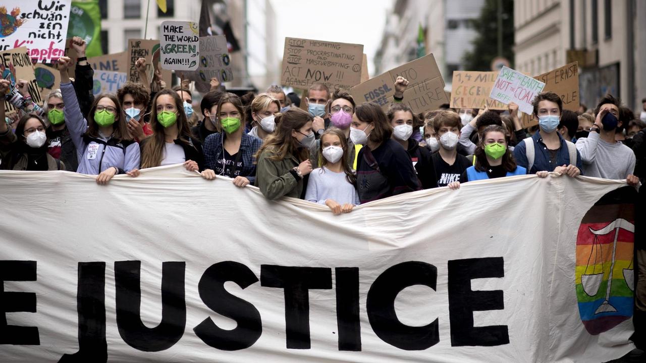 In Berlin demonstrieren viele junge Menschen gegen die Klimakrise. In der ersten Reihe steht Greta Thunberg hinter einem Banner mit der Aufschruft "Justice". In Berlin demonstrieren viele junge Menschen gegen die Klimakrise. In der ersten Reihe steht Greta Thunberg hinter einem Banner mit der Aufschruft "Justice".