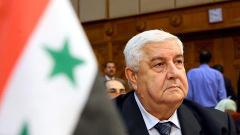 Außenminister Walid al-Mualem neben einer syrischen Flagge