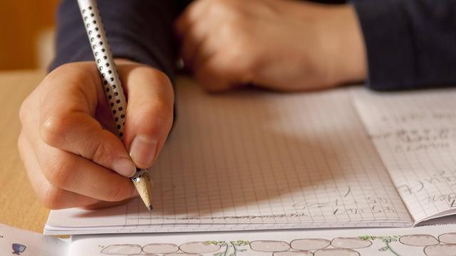 Eine Hand schreibt mit einem Stift auf einem Blatt Papier.