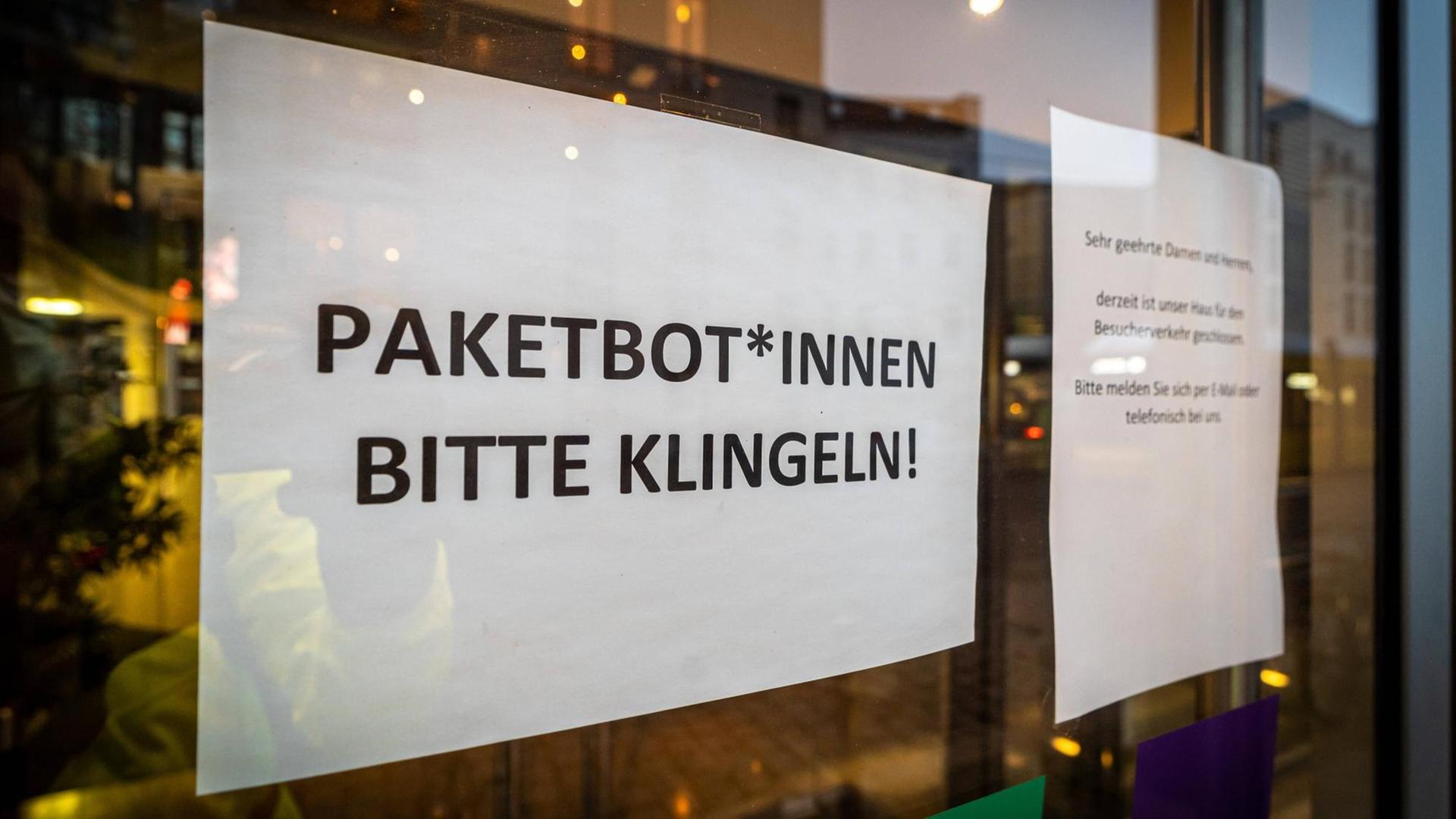 Ein Papier hinter einem Fenster, auf dem steht: "Paketbot*Innen Bitte Klingeln!" Ein Papier hinter einem Fenster, auf dem steht: "Paketbot*Innen Bitte Klingeln!"