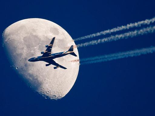 Ein Flugzeug fliegt über dem brandenburgischen Sieversdorf (Oder-Spree) scheinbar ganz nah am Mond vorbei.