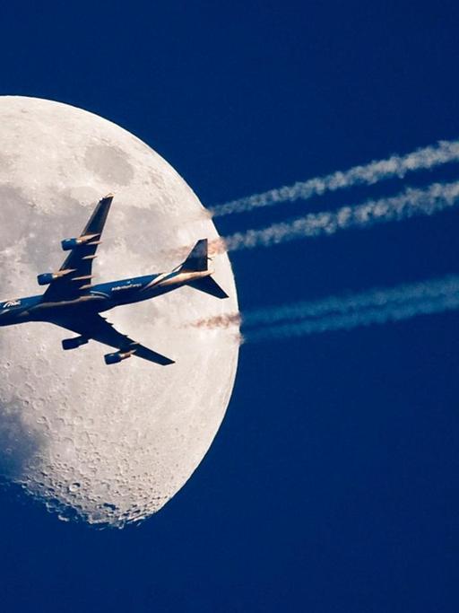 Ein Flugzeug fliegt über dem brandenburgischen Sieversdorf (Oder-Spree) scheinbar ganz nah am Mond vorbei.