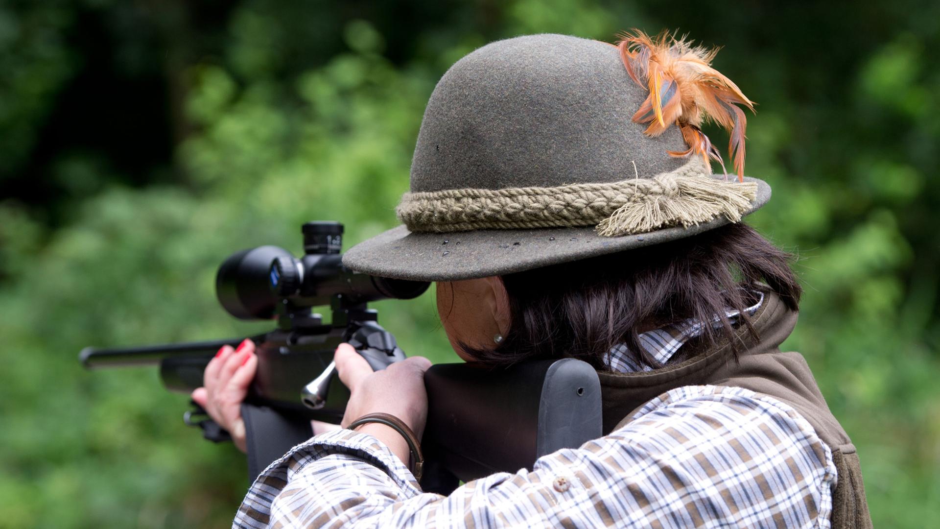 Eine Jägerin Andrea Wernick zielt mit einem Jagdgewehr und ist von hinten zu sehen.