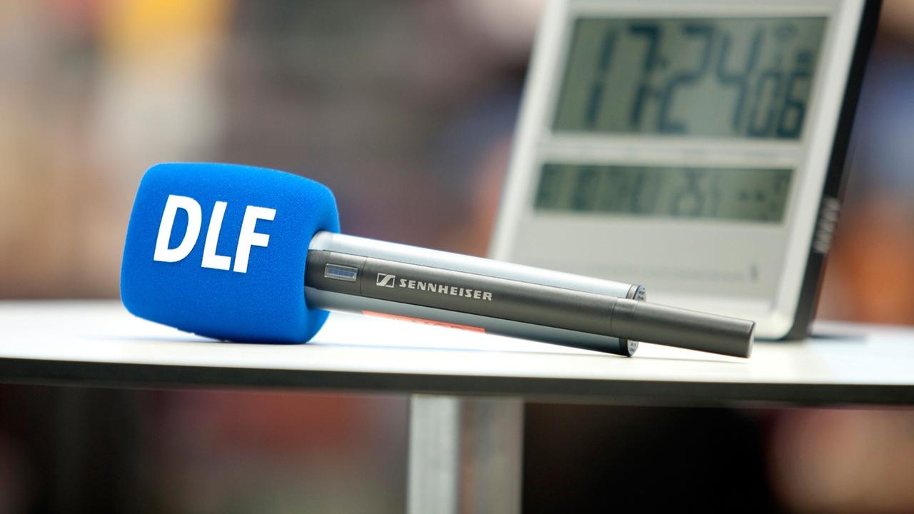 Ein DLF-Mikrofon liegt auf einem Tisch vor einer Digitaluhr. Ein DLF-Mikrofon liegt auf einem Tisch vor einer Digitaluhr.
