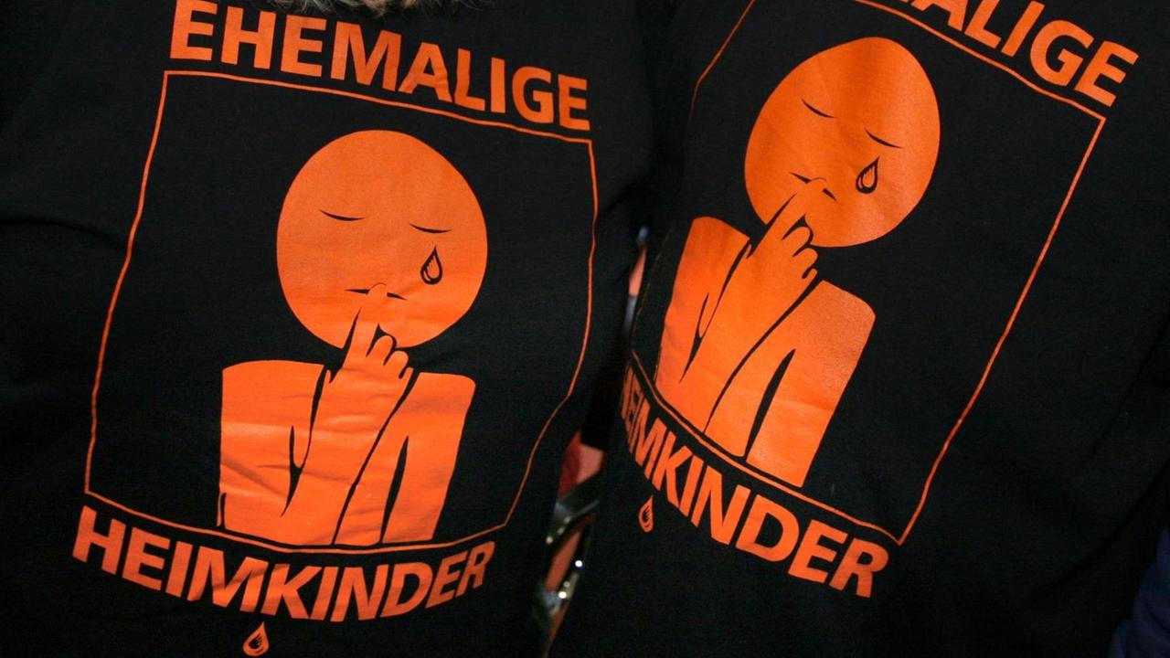 "Ehemalige Heimkinder" ist auf den T-Shirts eines Mannes und einer Frau zu lesen, auf denen auch eine weinende Figur aufgedruckt ist. "Ehemalige Heimkinder" ist auf den T-Shirts eines Mannes und einer Frau zu lesen, auf denen auch eine weinende Figur aufgedruckt ist.