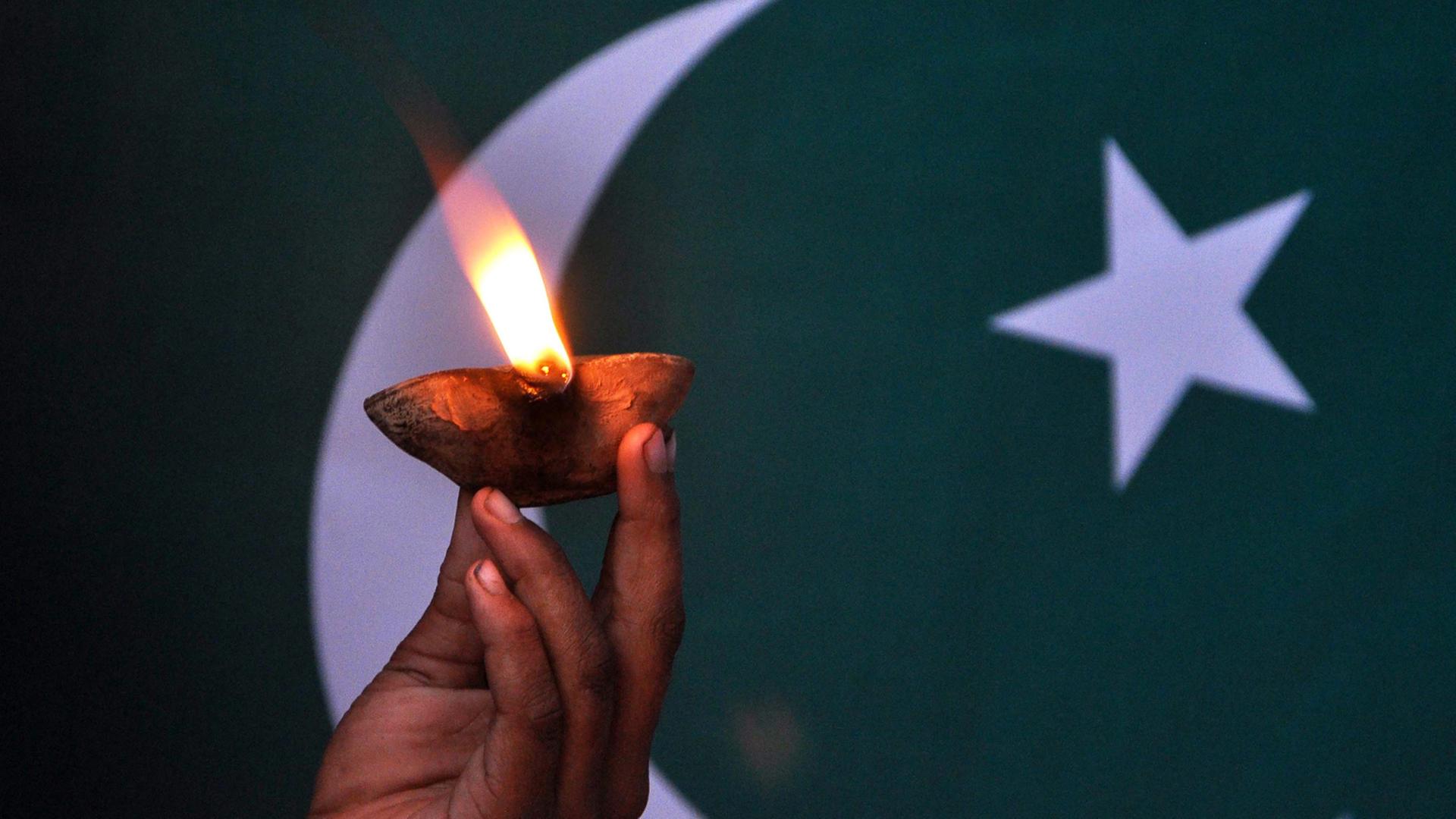 Eine Kinderhand hält eine Lampe vor der pakistanischen Flagge. Eine Kinderhand hält eine Lampe vor der pakistanischen Flagge.