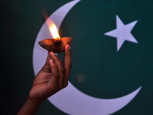 Eine Kinderhand hält eine Lampe vor der pakistanischen Flagge.