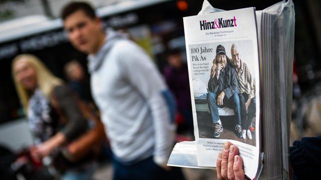 Der ehemalige Obdachlose Klaus hält vor einem Kaufhaus in Hamburg einen Stapel des Straßenmagazins "Hinz & Kunzt" in der Hand.