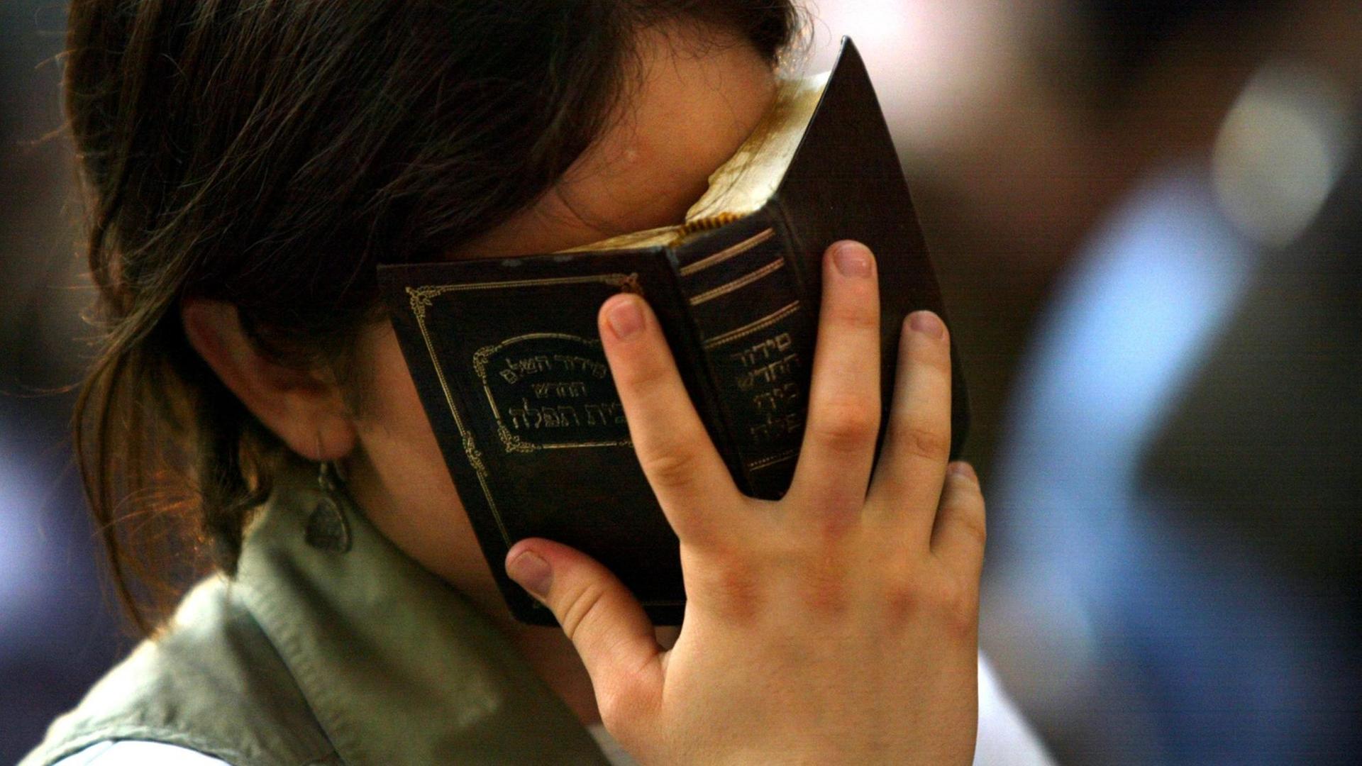 Eine israelische Frau rezitiert Gebete, während sie die Thora im frühen Abendlicht vor ihr Gesicht hält. Eine israelische Frau rezitiert Gebete, während sie die Thora im frühen Abendlicht vor ihr Gesicht hält.