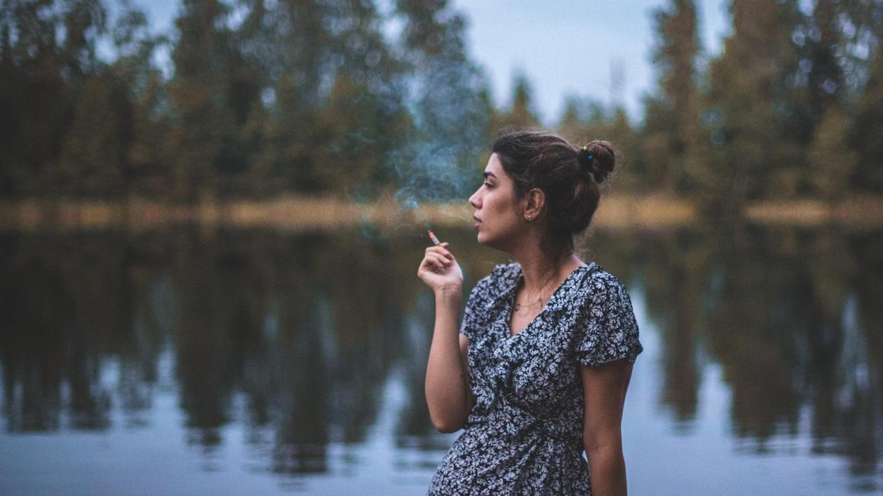 Eine junge Frau im Sommer steht an einem See und raucht. Eine junge Frau im Sommer steht an einem See und raucht.