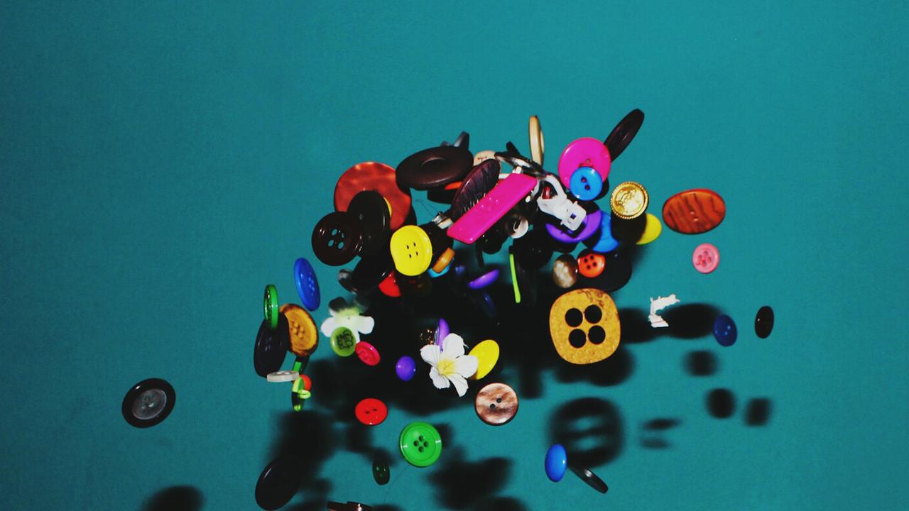 Vor einem grünen Hintergrund fliegen viele bunte Knöpfe durch die Luft. Vor einem grünen Hintergrund fliegen viele bunte Knöpfe durch die Luft.