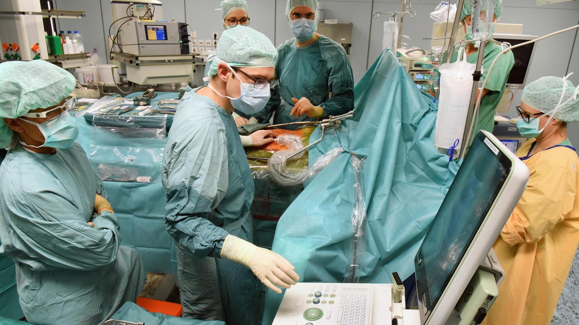 Eine Operation am Transplantationszentrum des Uniklinikums Leipzig. Medizinisches Personal in OP-Kleidung steht am OP-Tisch, eine Person bedient einen Computer. Eine Operation am Transplantationszentrum des Uniklinikums Leipzig. Medizinisches Personal in OP-Kleidung steht am OP-Tisch, eine Person bedient einen Computer.