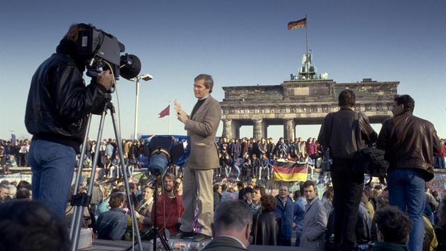 Ein Fernsehreporter berichtet am Brandenburger Tor über den Fall der Mauer.