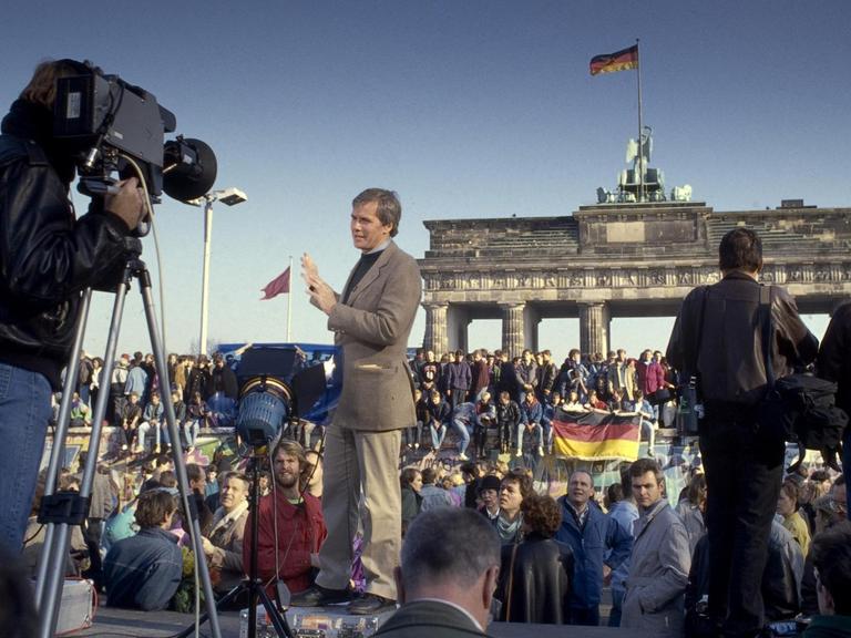 Ein Fernsehreporter berichtet am Brandenburger Tor über den Fall der Mauer.