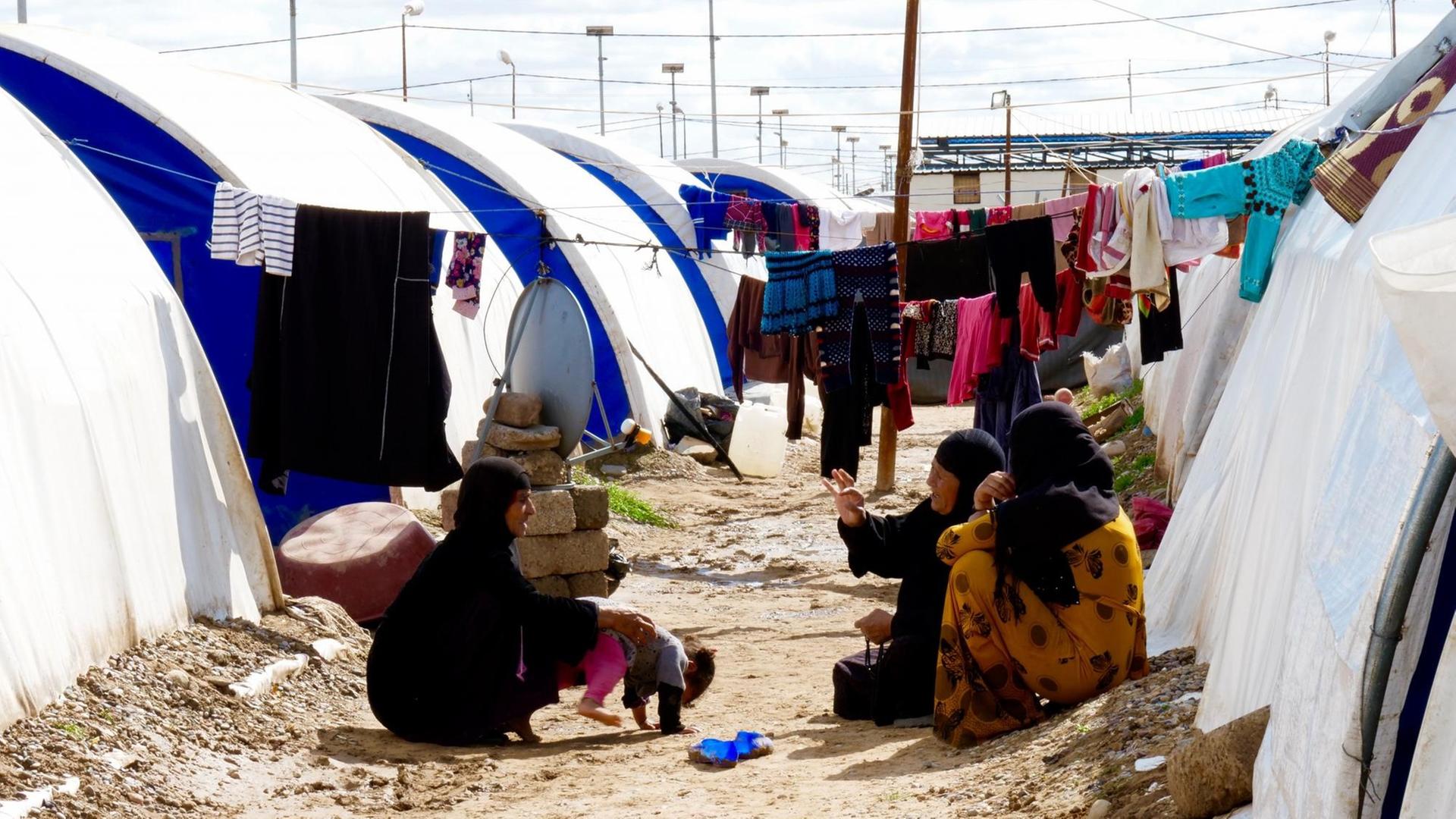Drei Frauen sitzen sich unterhaltend zwischen den Zelten im Jadah Lager, Kreis Mossul