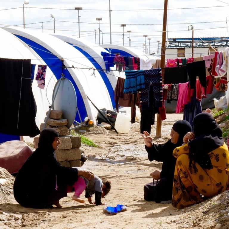 Drei Frauen sitzen sich unterhaltend zwischen den Zelten im Jadah Lager, Kreis Mossul
