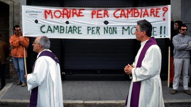 Priester bei einem Begräbniszug 1994 anlässlich des Todes eines von der Camorra erschossenen Priesters in Italien. Auf einem Transparent steht: "Sterben für Veränderung? Veränderung, um nicht zu sterben!!"
