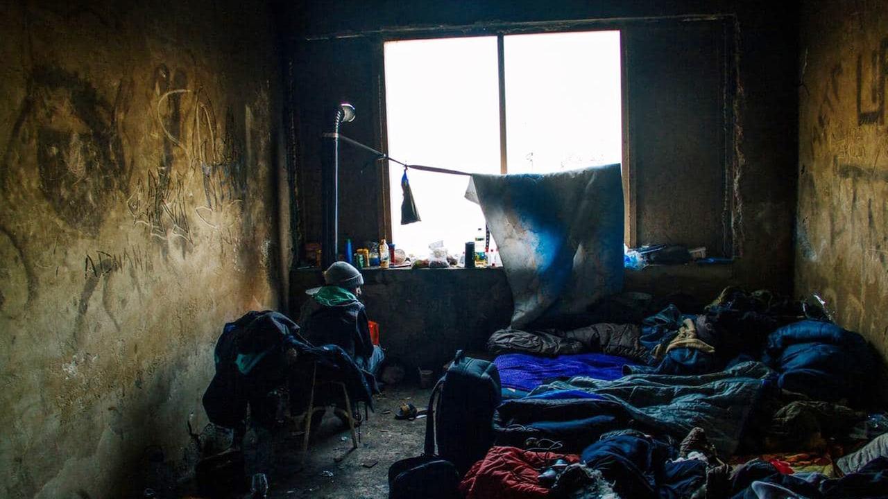 Ein Flüchtling an der bosnisch-kroatischen Grenze sitzt in einem abbruchreifen Haus in einem kalten Zimmer, umgeben von vielen Schlafsäcken. Ein Flüchtling an der bosnisch-kroatischen Grenze sitzt in einem abbruchreifen Haus in einem kalten Zimmer, umgeben von vielen Schlafsäcken.