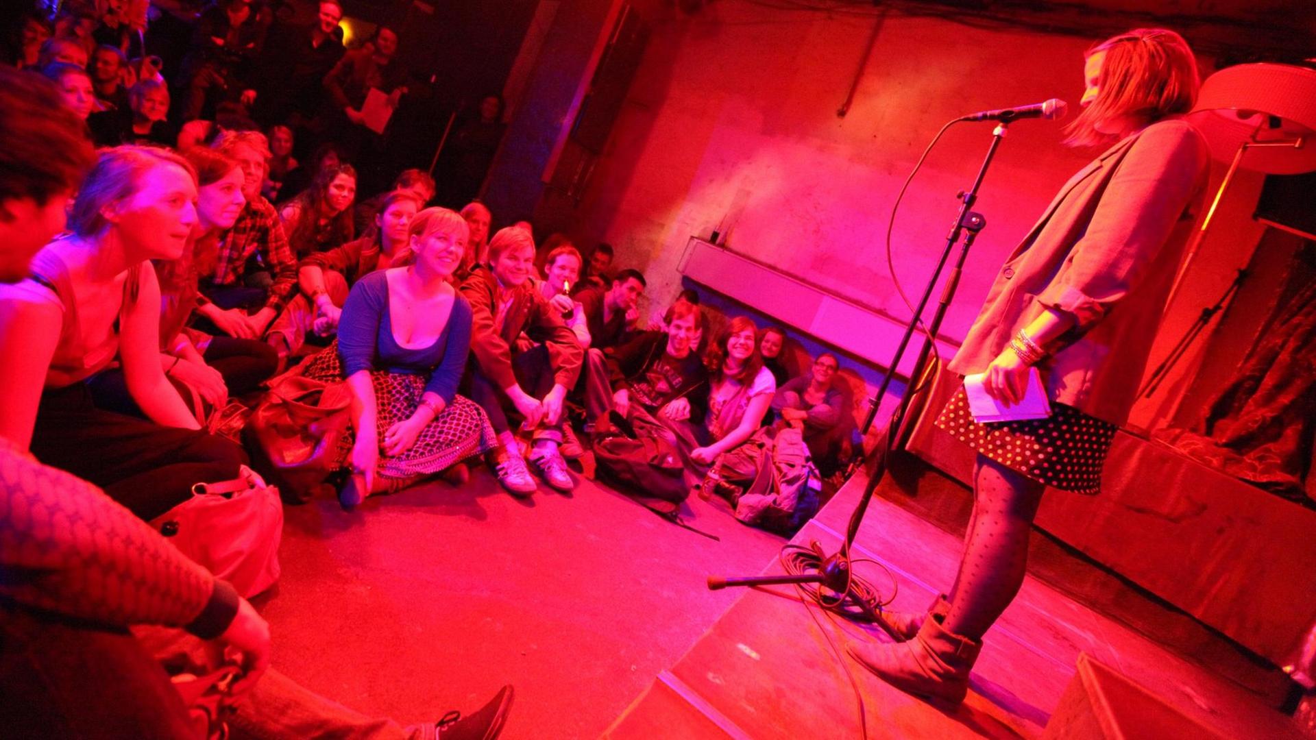 Gäste hören im Club "Rosi's" in Berlin-Friedrichshain bei einem "Poetry Slam" zu. Auf der Bühne rezitiert eine Autorin am Mikrofon ihren Text.