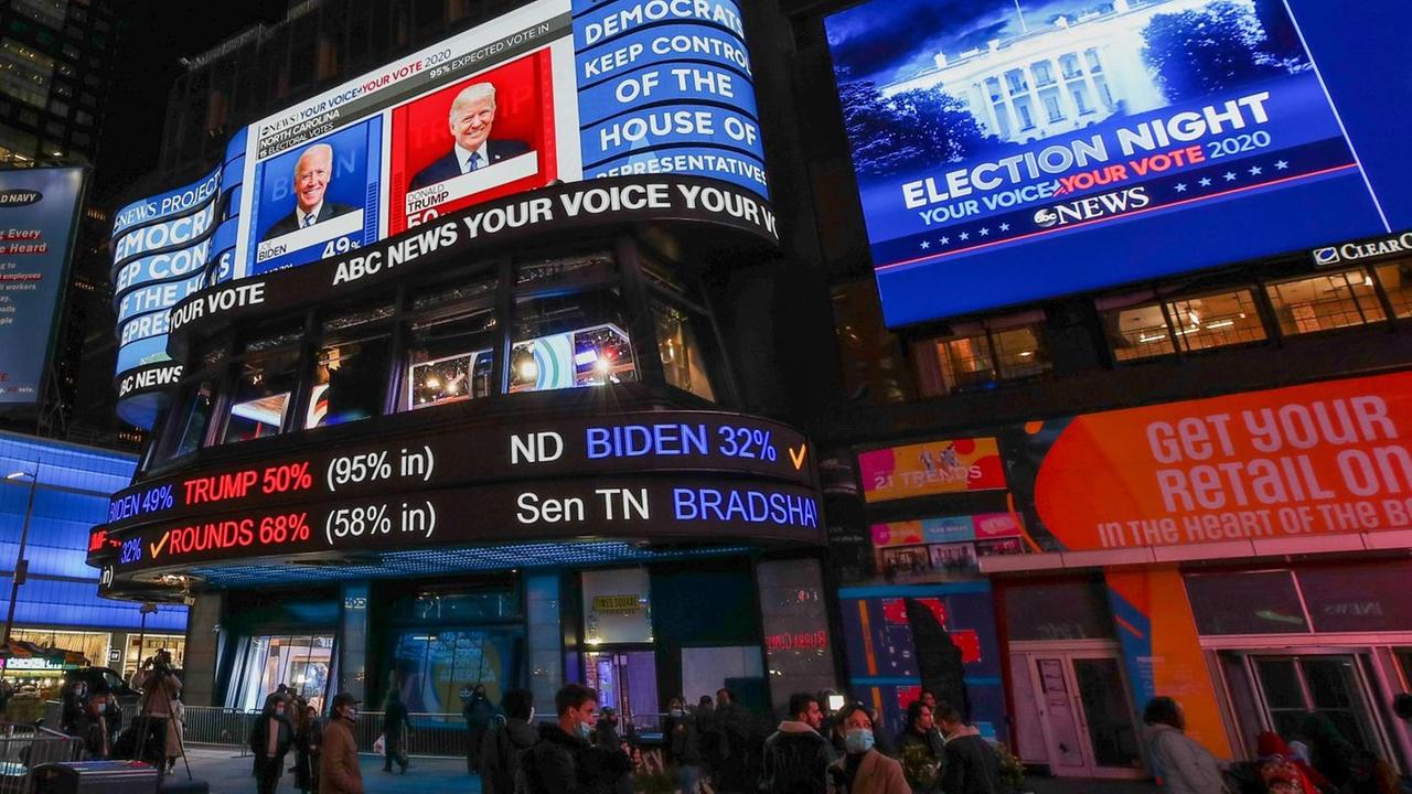 Menschen auf dem Times Square schauen auf riesige Bildschirme, die Donald Trump und Joe Biden sowie die Zahlen der Wahl zeigen. Menschen auf dem Times Square schauen auf riesige Bildschirme, die Donald Trump und Joe Biden sowie die Zahlen der Wahl zeigen.