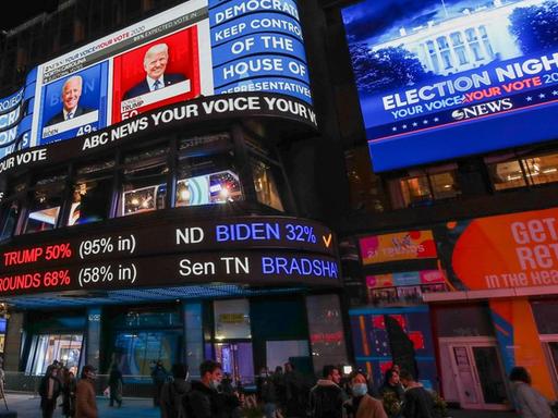 Menschen auf dem Times Square schauen auf riesige Bildschirme, die Donald Trump und Joe Biden sowie die Zahlen der Wahl zeigen.