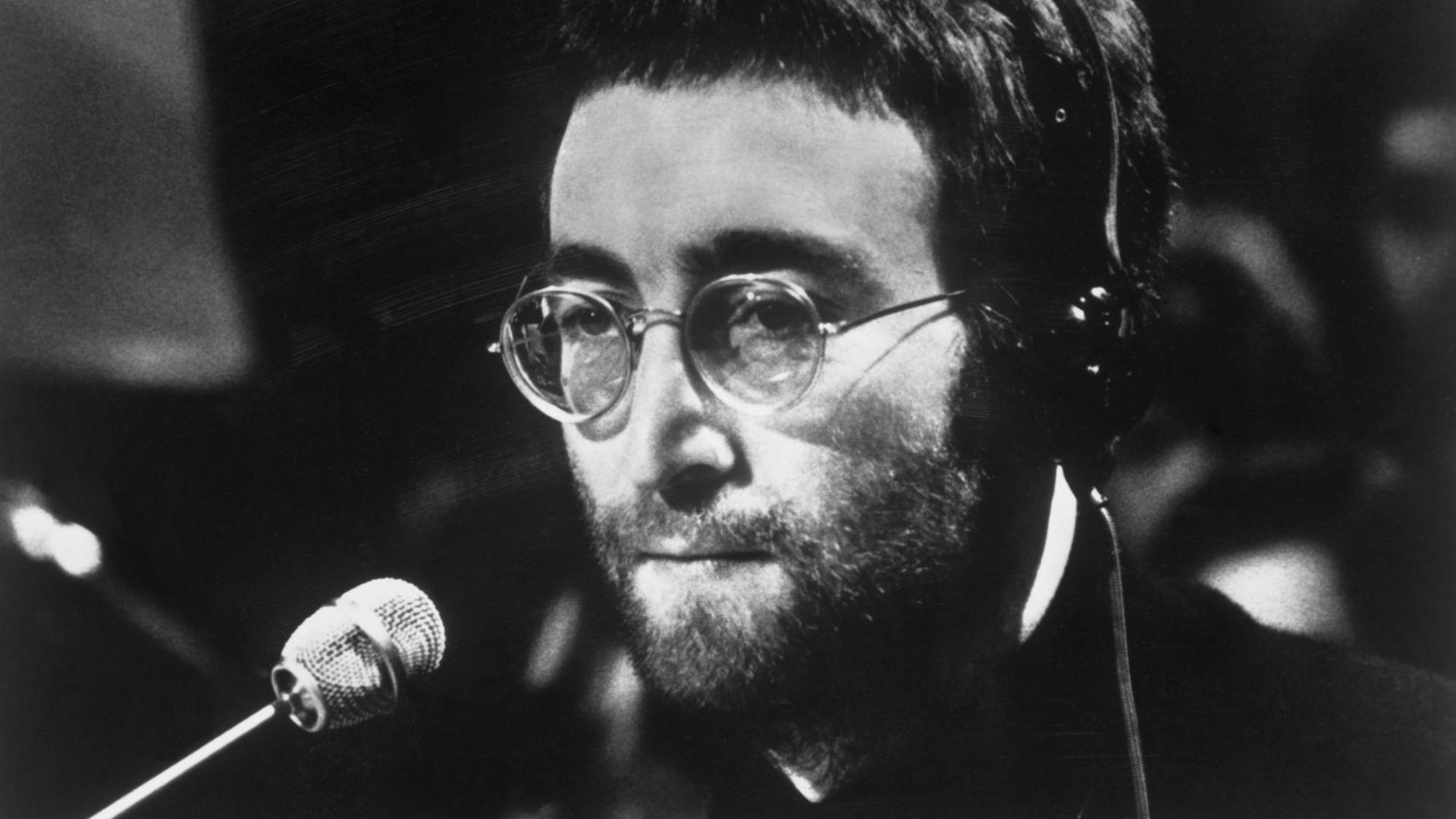 Schwarzweiß Aufnahme von John Lennon mit Kopfhörern und am Mikrofon