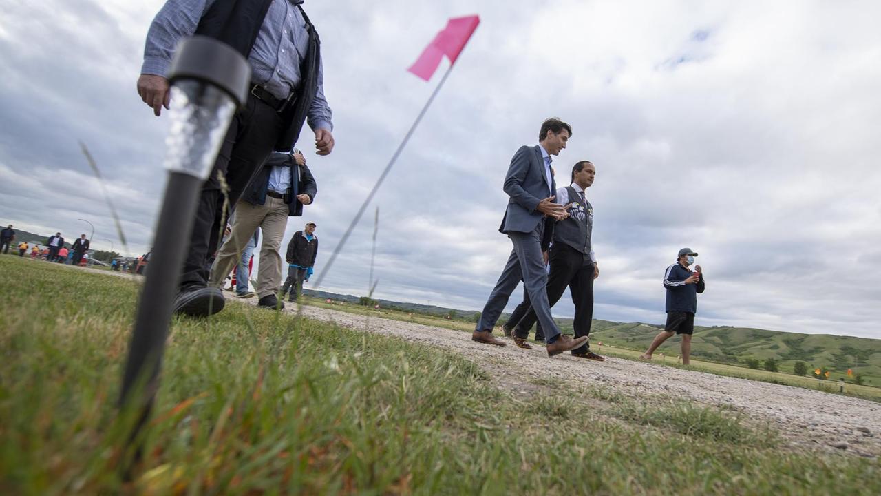 Kanadas Premier Justin Trudeau im Anzug in Begleitung beim Laufen über ein Gelände, wo einst ein Internet für indigene kanadische Kinder stand