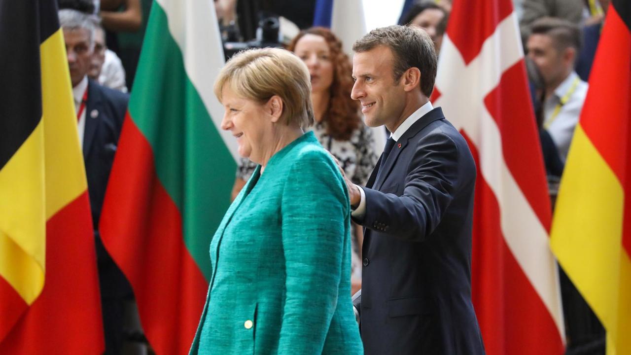 Merkel und Macron gehen an den Flaggen der Mitgliedsstaaten vorüber Merkel und Macron gehen an den Flaggen der Mitgliedsstaaten vorüber