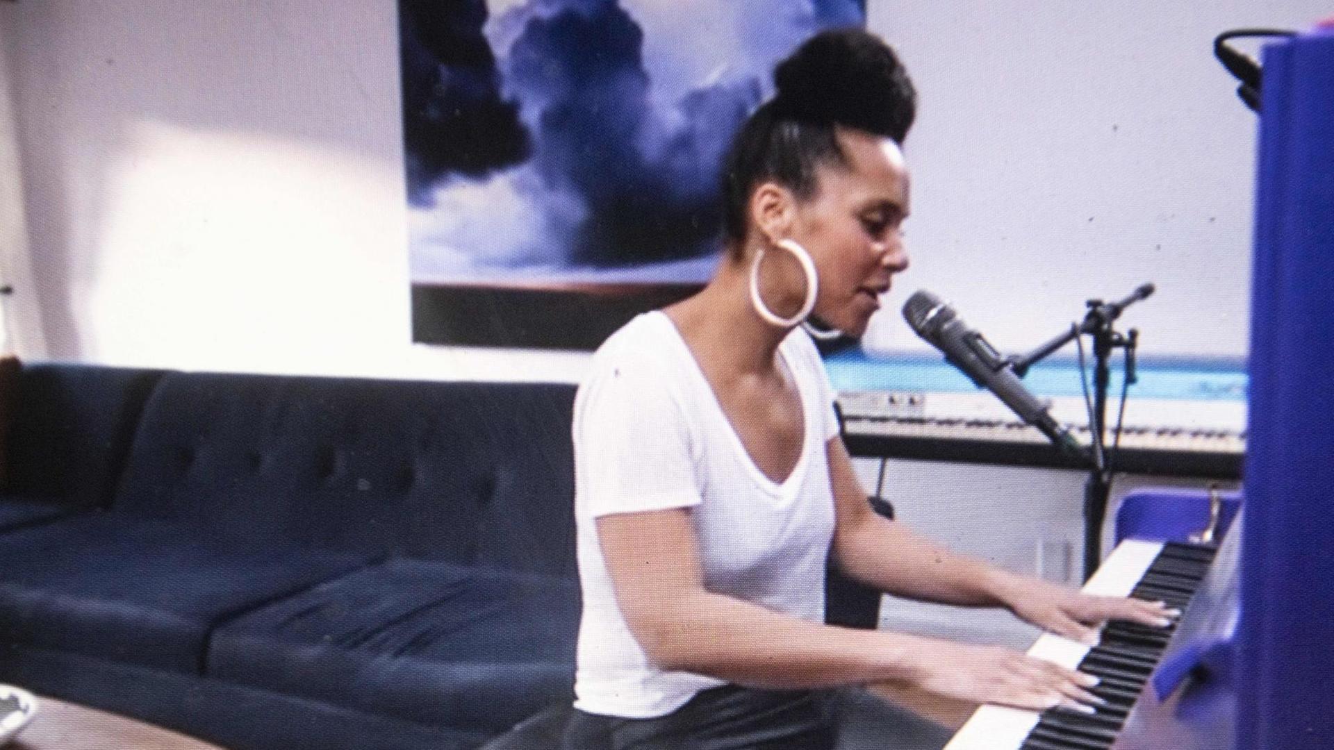 Alicia Keys am Klavier. Im Hintergrund ein Sofa. Alicia Keys am Klavier. Im Hintergrund ein Sofa.