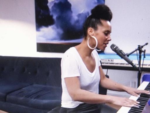 Alicia Keys am Klavier. Im Hintergrund ein Sofa.