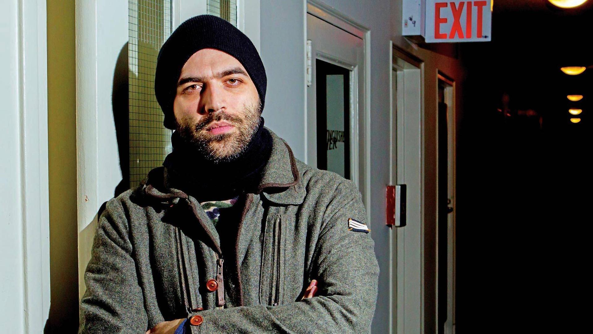 Farbfoto eines jungen bärtigen Mannes mit Mütze in einem dunklen Hausflur. Es ist der italienische Journalist und Buchautor Roberto Saviano Farbfoto eines jungen bärtigen Mannes mit Mütze in einem dunklen Hausflur. Es ist der italienische Journalist und Buchautor Roberto Saviano