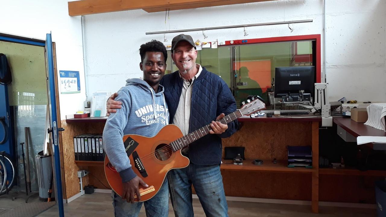 Matthias Köppen und Shumay halten gemeinsam eine Gitarre Matthias Köppen und Shumay halten gemeinsam eine Gitarre