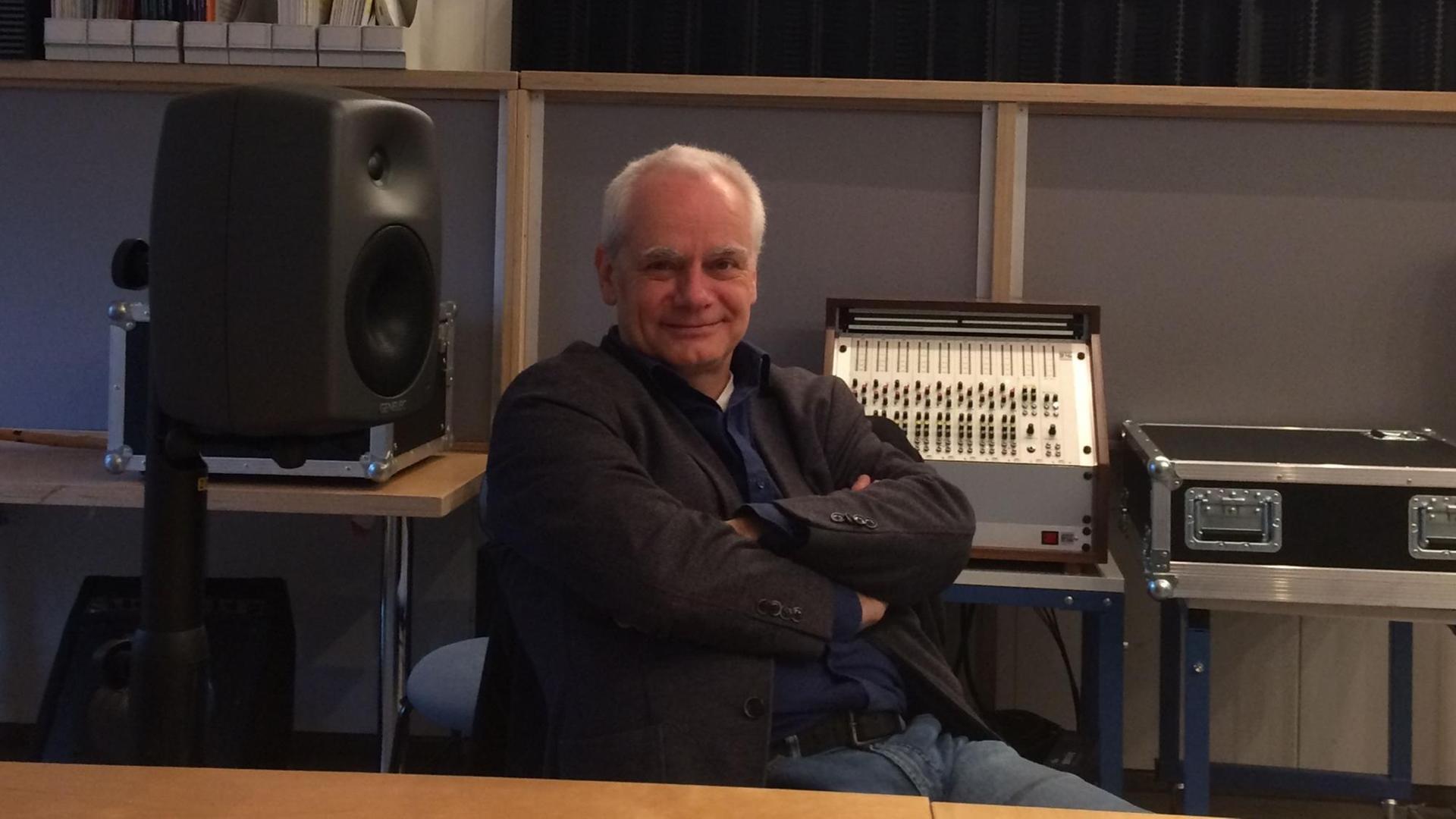 Ein Mann sitzt inmitten eines Studios mit verschränkten Armen und lächelt in die Kamera. Ein Mann sitzt inmitten eines Studios mit verschränkten Armen und lächelt in die Kamera.