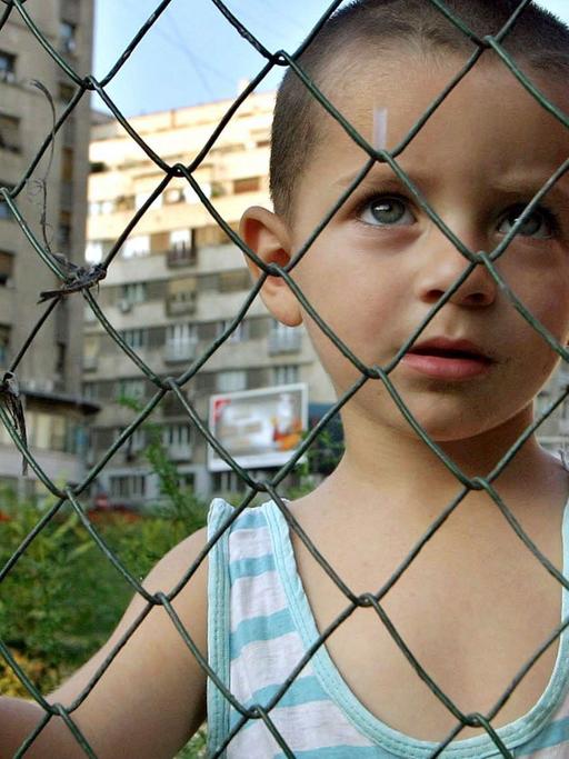 Ein rumänischer Junge schaut in Bukarest durch einen Maschendrahtzaun.