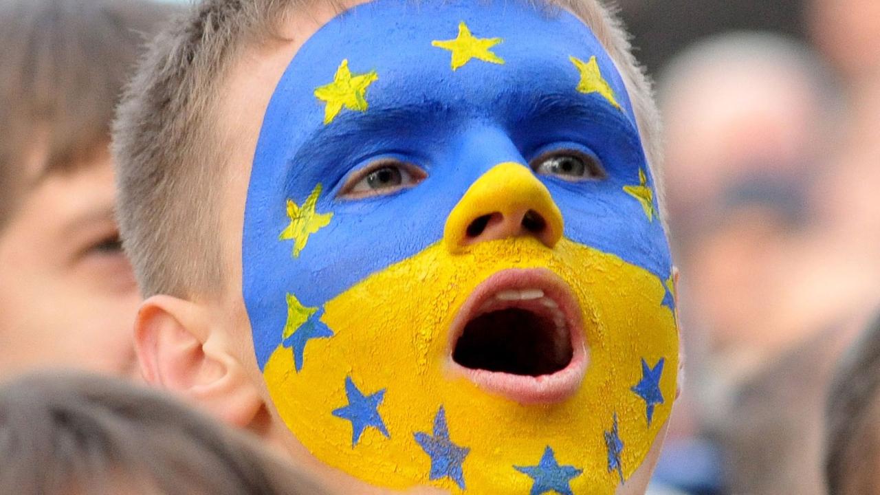 Ein Junge mit einer ins Gesicht gemalten gelb-blauen ukrainischen Flagge, auf der auch die Sterne der EU-Fahne zu sehen sind. Ein Junge mit einer ins Gesicht gemalten gelb-blauen ukrainischen Flagge, auf der auch die Sterne der EU-Fahne zu sehen sind.