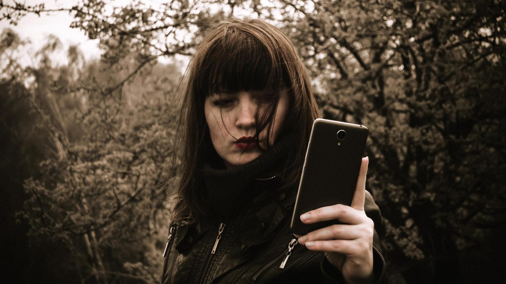 Eine Frau steht im Wald und schaut auf ihr Smartphone. Eine Frau steht im Wald und schaut auf ihr Smartphone.