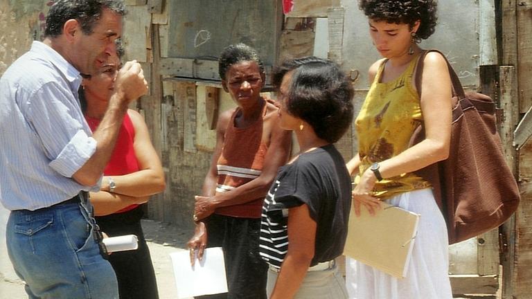 Eine Gruppe Leute steht in einem brasilianischen Elendsviertel und diskutiert mit den Bewohnern. Eine Gruppe Leute steht in einem brasilianischen Elendsviertel und diskutiert mit den Bewohnern.