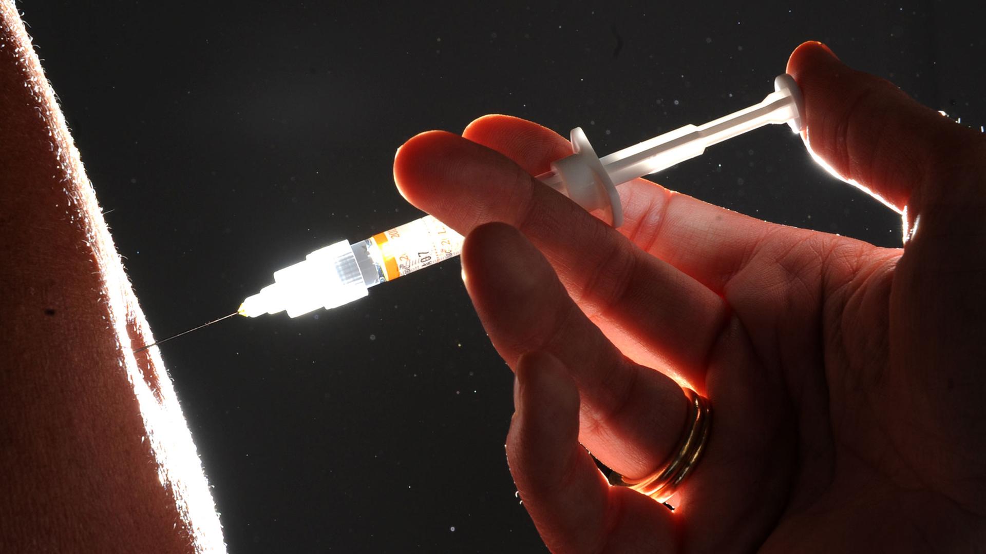Eine Spritze sticht in einen Arm Eine Spritze sticht in einen Arm
